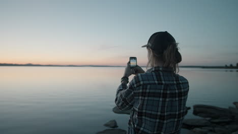 Woman-Photographing-Sunset-over-Lake-with-Smartphone